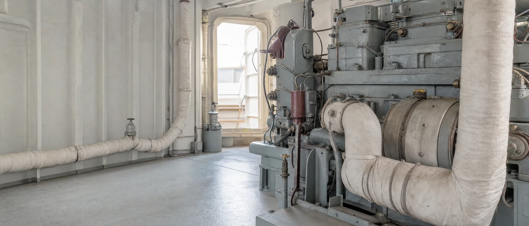 Old shipyard engine room with runs of asbestos pipe insulation, the kind of work site behind many asbestos trust fund claims